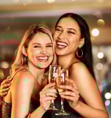 Two women laughing and clinking champagne glasses during a vibrant night out in downtown Las Vegas.