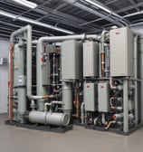 An outdoor air conditioning unit is mounted on a textured wall with various pipes and electrical conduits running above it. The unit is labeled GREE and is connected to a green hose. Below, several empty black plastic crates are stacked haphazardly on a rough concrete surface.