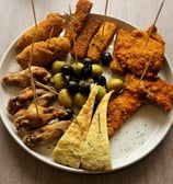 Restaurant table with a complete meal set featuring crispy croquettes, golden fries with aioli, arti