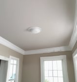 Two people are working on the exterior of a building, seemingly painting or repairing it. The building is surrounded by a framework of bamboo scaffolding. The sky is a soft gradient of pale yellow to orange, suggesting either early morning or late evening. The building itself is painted in light blue and has some decorative elements in darker shades.