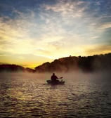 a man in a kayak on a lake at sunset