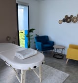 a massage table with a blue chair and a yellow chair