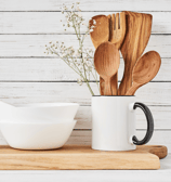 Wood spoons and laddles placed in a coffee cup with ceramic bowls besides.