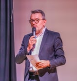 Un animateur de conférence avec un micro et des fiches dans les mains qui parle