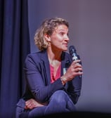 Femme avec un micro assise qui parle pendant une conférence
