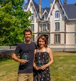 Un homme et une femme qui posent en souriant avec un trophée devant un chateau
