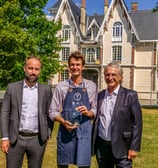 Trois personnes qui posent devant un château avec un trophée en souriant