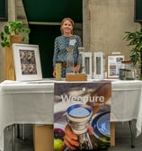 Femme qui pose derrière son stand qui présente des carafes d'eau filtrantes naturelles