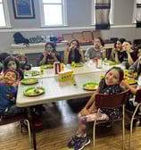 a group of children sitting at a table with plates of food