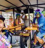 a man and woman sitting at a table of Riga Beer Bike with a man in a colorful costume