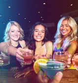 Group of smiling women toasting cocktails across the bar during a girls’ night out in downtown Las Vegas.