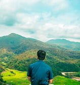 Homme de dos assis en montagne regardant une vallée et les sommets verdoyants