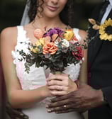 A Hertfordshire bride in a white dress holding a bouquet of paper flowers, standing outdoors.