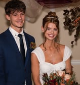 Smiling bride and groom pose indoors with floral bouquet and autumn-themed decor.
