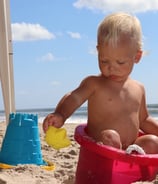 photographer portrait of a baby in a pink bucketle on a beach