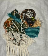 fabric collage with sequins in shades of green, teal, rust, black and cream; cat face and lace used