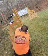 Kneeling man engaging targets from a barrier using self-defense firearm during training.