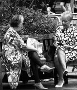 Two women sit on a bench, chatting, on a sunny day at Festival Square, Lothian Road, Edinburgh