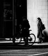 A woman on her bike, in shadow, and a woman behind her in the light at the bottom of Morningside Road, Edinburgh