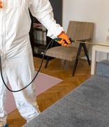 a man in a white suit and orange gloves is spraying a couch