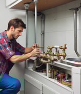 The image captures the top part of an emergency vehicle with a focus on its blue emergency lights and sirens. The vehicle features a white and orange color scheme. Behind it, there is a dark-tiled roof and a wall with windows that suggest a residential area.