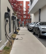 A network patch panel with numerous green fiber optic connectors arranged in a row. Bright yellow cables are plugged into each connector, extending outwards in an organized manner. The cables and connectors appear to be part of a structured cabling system in a data center or similar technical environment.