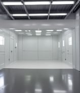The interior of a factory or assembly line is visible, with several workstations lined up neatly. Each station contains white plastic enclosures with electronic components inside, suggesting an electronic manufacturing or assembly process. Overhead lighting and blue tool boards are present, with some orange coiled cords hanging down.
