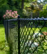 a black chain link fence with flowers in the background