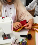 Couturière mesurant un tissu rouge à la main avec un ruban de mesure, illustrant la création