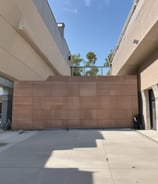 An interior wall is covered with a grid of beige tiles. Several electrical conduits run vertically and horizontally across the surface, connecting multiple junction boxes affixed to the wall. One of the boxes is marked with the letter 'N'. The overall appearance is industrial and functional.