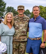 Two parents standing with their son who is in Army camoflage.  They are with other families.