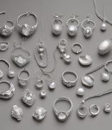 A storefront adorned with green garlands and pink flowers framing the entrance of a jewelry shop. The stone facade features detailed masonry, and there's a sign displaying 'V. Vittoria Jewels'. The entrance door is open, revealing part of the interior, and a large potted plant is positioned nearby.