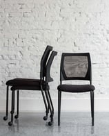 Stacked and upright V137 chairs against a white brick wall, front and side view