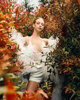 Portrait of model in a white lace top surrounded by red flowers in Bali, styled for a fashion editorial.