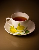 A commercial shot of a hand-painted cup on a saucer, filled with steaming black tea