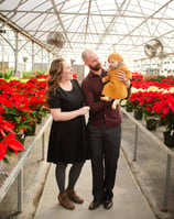 a man and woman holding a baby in a greenhouse