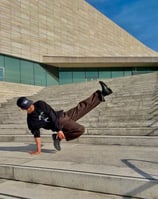 YoYo performing a breakdance move in front of concrete building.