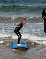 A young girl taking a surf lesson riding a blue surfboard on the water