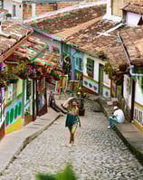 Una Mujer paseando por una calle tradicional de Guatapé, con sus casas adornadas con zocalos