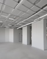 A white wall with two vent openings casting shadows. There is a yellow caution sign with Chinese characters and a telephone number, along with a small mailbox or utility box attached to the wall.