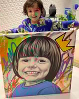 Imagem de uma criança feliz, segurando uma pintura do seu rosto.
