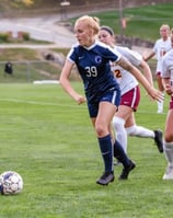 Female soccer player in blue jersey number 39 dribbling the ball during a college match.