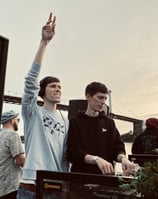 Two dj men standing in front of a large screen