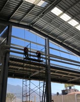 Trabajadores instalando tuberías aéreas en el techo de una nave industrial.