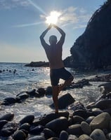a man performing yoga on rocks in the sea