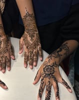 two hands rest next to each other on a table with intricate designs on them, one henna and one jagua