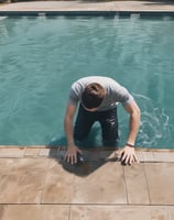 A swimming pool with clear, rippling water reflecting the light. At the bottom, a large, abstract design is visible, featuring a combination of green and aqua hues against a red-tiled background.
