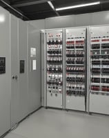 A close-up view of a network server rack filled with multiple fiber optic cables and connectors. The cables are predominantly yellow and green, some labeled with tags, and they are connected to various ports and modules. The setup appears highly organized and is likely part of a data center or telecommunications infrastructure.