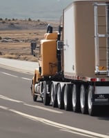 A large flatbed truck is driving down a highway, carrying a long, red industrial component. The sky is bright with scattered clouds, and tall trees line the side of the road. Several cars are also visible on the highway.