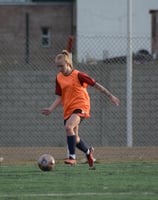 Female soccer player in an orange training vest dribbling the ball during a practice session.